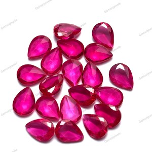 May include: A collection of faceted, pear-shaped rubies in varying sizes, displaying a vibrant, deep pink-red hue. The gemstones are scattered on a white surface, with the text "Gemsnjewele" repeated around the edges.
