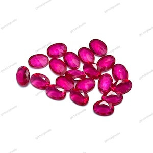 Könnte beinhalten: Eine Ansammlung oval geschliffener, leuchtend roter Edelsteine. Die Edelsteine sind auf weißem Hintergrund angeordnet und zeigen ihre polierten Oberflächen und ihren inneren Glanz. Der Text "gemsnjewele" ist im Hintergrund enthalten.