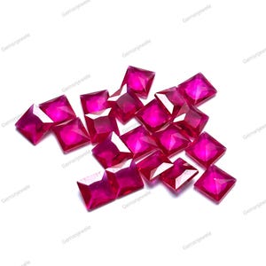Könnte beinhalten: Eine Ansammlung leuchtend roter, quadratisch geschliffener Edelsteine. Die Edelsteine sind auf weißem Hintergrund verstreut, wodurch ihre Facetten und ihre satte Farbe zur Geltung kommen. Das Bild ist gut beleuchtet und unterstreicht die Klarheit und Brillanz der Steine. Der Text "Gemsnjewele" ist wiederholt.