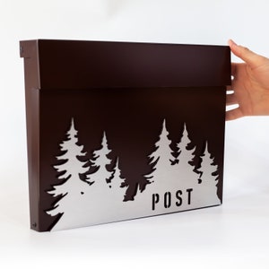May include: A brown metal mailbox with a silver metal front panel featuring a cut-out design of a forest with trees and the word "POST".