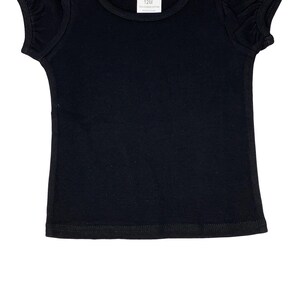 May include: A black short-sleeved t-shirt with puffed sleeves. The shirt has a round neckline and a tag that reads "AJ Blanks 12M 100% Combed Cotton Made in China."