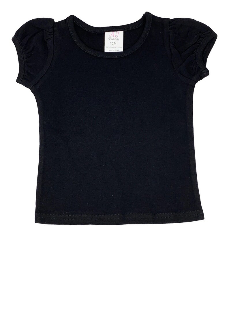 May include: A black short-sleeved t-shirt with puffed sleeves. The shirt has a round neckline and a tag that reads "AJ Blanks 12M 100% Combed Cotton Made in China."