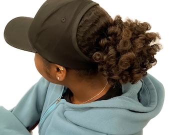 May include: A black baseball cap with a ponytail hole in the back. The cap is worn by a person with curly brown hair.