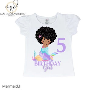 May include: White t-shirt with a purple number 5, the words "birthday girl" and a cartoon illustration of a Black mermaid with a pink star in her hair.