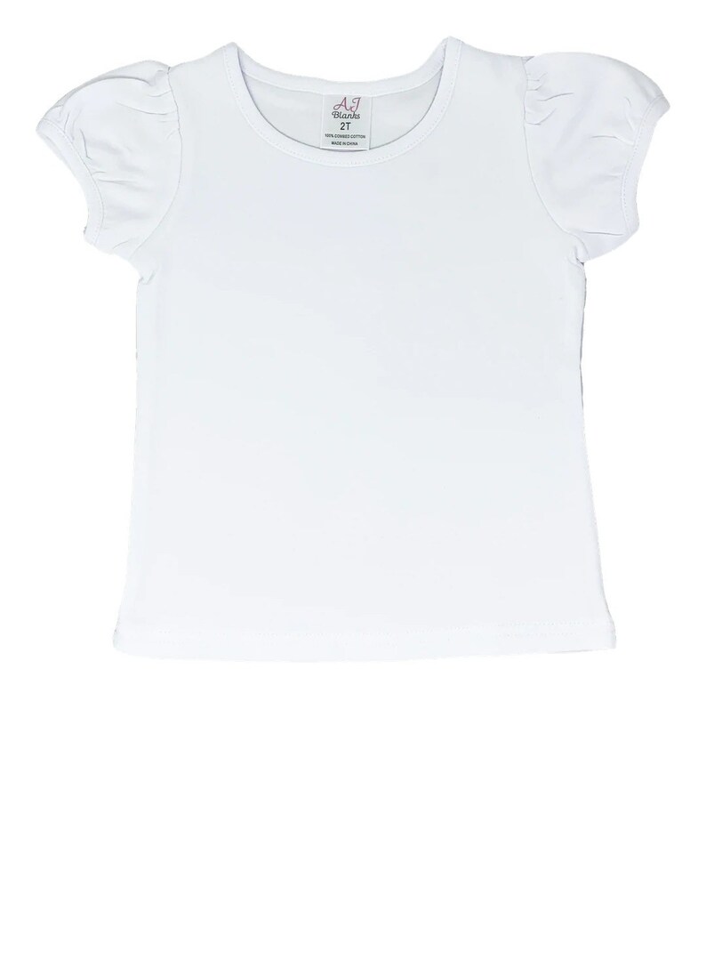 May include: White short-sleeved t-shirt with puffed sleeves. The shirt has a round neckline and a small tag that says "AJ Blanks 2T 100% combed cotton Made in China".