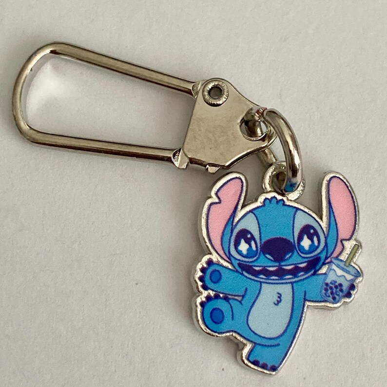 Puede incluir: Un llavero de Stitch azul y rosa con un cierre plateado. El personaje de dibujos animados sostiene una bebida. Un accesorio divertido para los fans de la pel&iacute;cula animada.