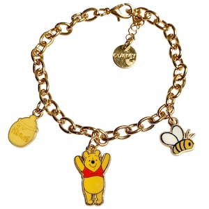 May include: Gold-coloured charm bracelet with Winnie the Pooh, a honey pot, and a bee charms. The bracelet has a chain link design and a round Disney charm. The Winnie the Pooh charm is yellow with a red shirt.