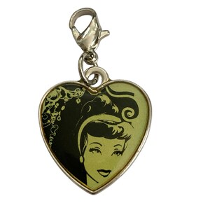 May include: A silver heart-shaped charm with a black and white image of a woman with a green background. The charm has a silver clasp.