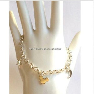 Puede incluir: Pulsera de cadena de plata con un dije de Mickey Mouse dorado, un dije de luna creciente y un dije de estrella. South Miami Beach Boutique.