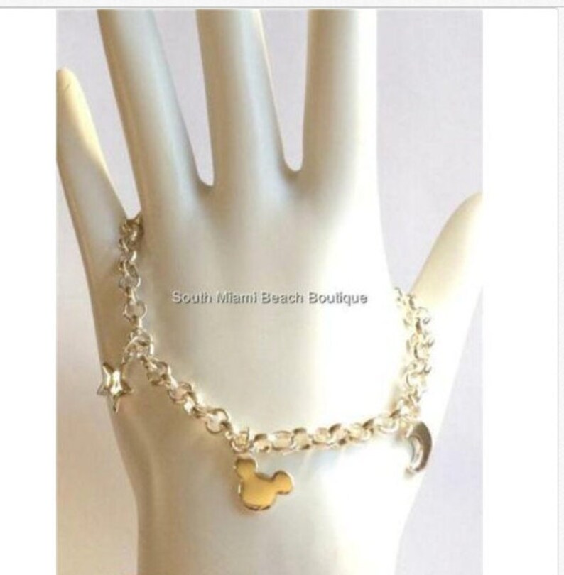 Puede incluir: Pulsera de cadena de plata con un dije de Mickey Mouse dorado, un dije de luna creciente y un dije de estrella. South Miami Beach Boutique.