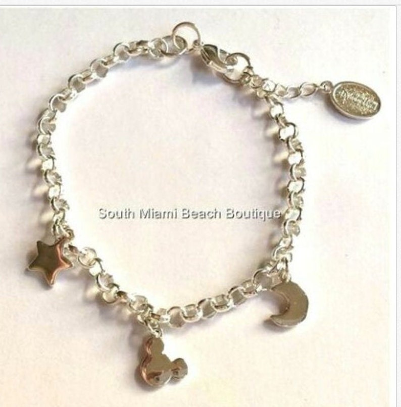Puede incluir: Un brazalete de plata con un encanto de estrella, media luna y Mickey Mouse. El brazalete tiene un cierre de langosta y una peque&ntilde;a etiqueta con el texto "South Miami Beach Boutique".