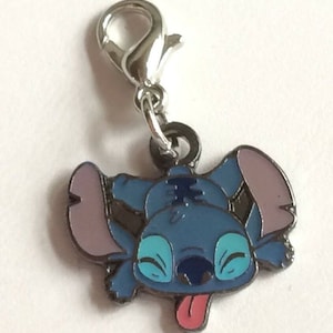 May include: A silver charm with a blue Stitch character from the Disney movie Lilo & Stitch. Stitch is shown with his tongue sticking out and his eyes closed.