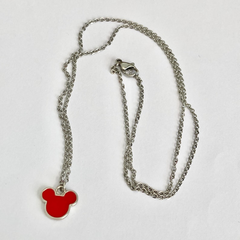 K&ouml;nnte beinhalten: Eine silberne Kettenkette mit einem roten Mickey Mouse Kopf Anh&auml;nger.