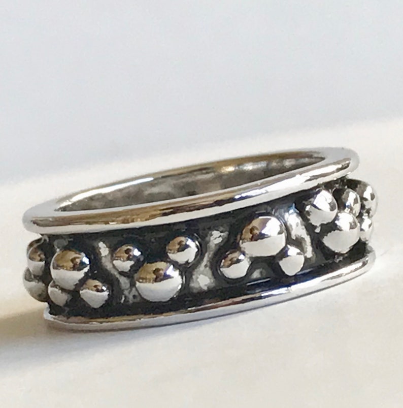 Puede incluir: Un anillo plateado con un dise&ntilde;o texturizado. El anillo presenta una banda de peque&ntilde;as esferas elevadas entre dos bandas lisas y pulidas. Las esferas tienen un aspecto met&aacute;lico reflectante.