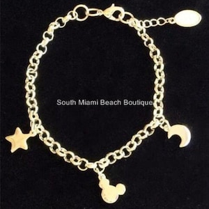 Puede incluir: Pulsera de cadena dorada con tres dijes: una estrella, una luna creciente y una cabeza de Mickey Mouse.