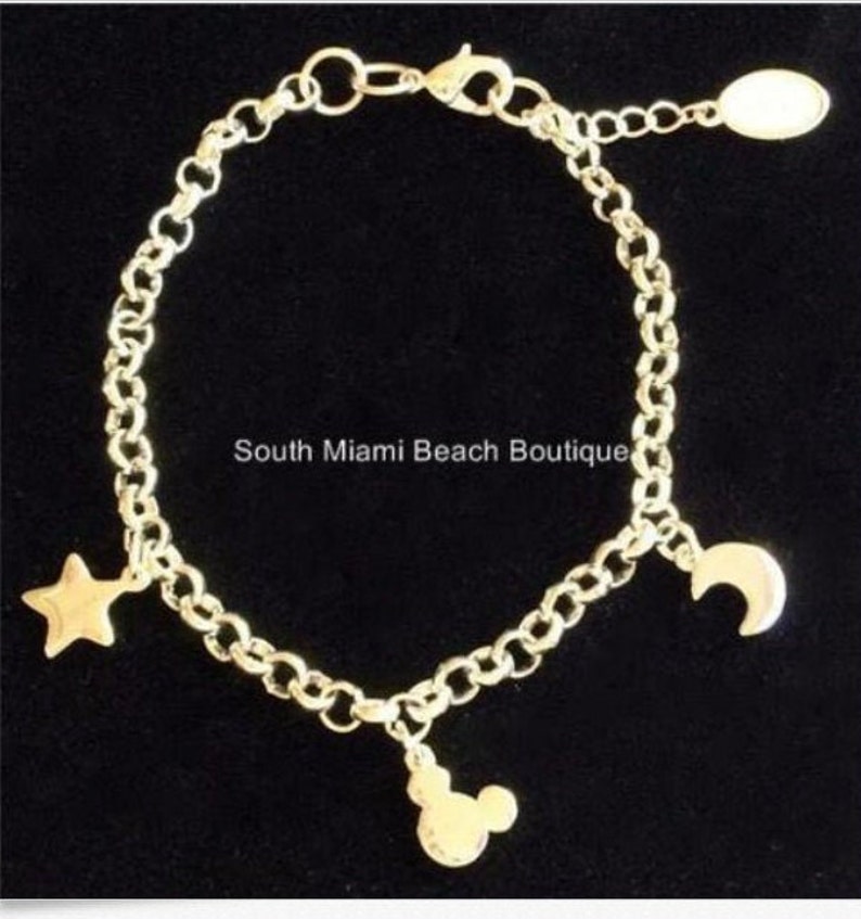 Puede incluir: Pulsera de cadena dorada con tres dijes: una estrella, una luna creciente y una cabeza de Mickey Mouse.