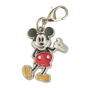 May include: A Mickey Mouse charm with a silver clasp. The charm features a smiling Mickey Mouse in his classic outfit: red shorts, yellow shoes, and black body and ears. The charm is made of metal and enamel.