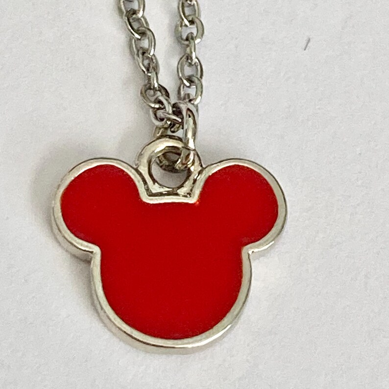 K&ouml;nnte beinhalten: Eine silberne Kettenkette mit einem roten Mickey Mouse Kopf Anh&auml;nger.