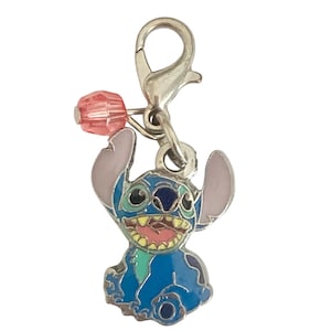 Puede incluir: Un charm de esmalte azul con el personaje Stitch de Lilo & Stitch. El charm tiene un cierre plateado y una cuenta rosa. Stitch sonr&iacute;e con la lengua rosa y tiene orejas grandes. Adecuado para pulsera o collar.