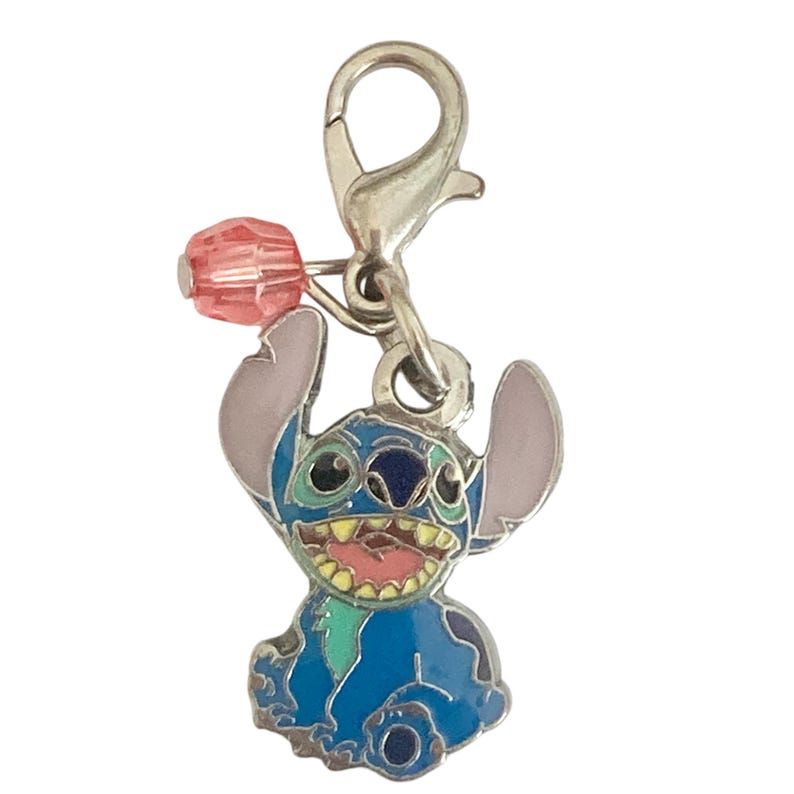Puede incluir: Un charm de esmalte azul con el personaje Stitch de Lilo & Stitch. El charm tiene un cierre plateado y una cuenta rosa. Stitch sonr&iacute;e con la lengua rosa y tiene orejas grandes. Adecuado para pulsera o collar.