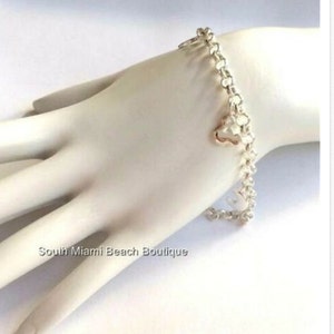 Puede incluir: Un brazalete de cadena de plata con un peque&ntilde;o dije en forma de coraz&oacute;n. El brazalete est&aacute; sobre una superficie blanca.