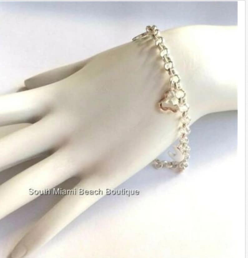 Puede incluir: Un brazalete de cadena de plata con un peque&ntilde;o dije en forma de coraz&oacute;n. El brazalete est&aacute; sobre una superficie blanca.