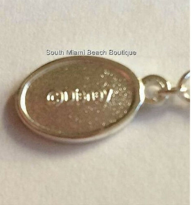 Puede incluir: Primer plano de una etiqueta ovalada de plata con la palabra "GUESS" grabada en ella.