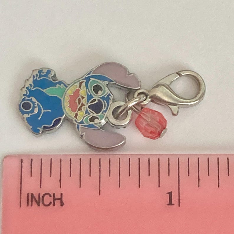 Puede incluir: Un charm plateado con un cierre de mosquet&oacute;n, con un dise&ntilde;o de personaje de dibujos animados colorido. El charm tiene detalles de esmalte azul, rosa y amarillo, con una peque&ntilde;a cuenta roja. El charm mide aproximadamente 2,5 cm de largo.