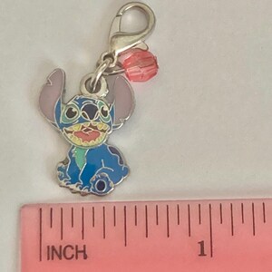 Puede incluir: Un charm azul y plateado con el personaje Stitch de Lilo & Stitch. El charm tiene un cierre de mosquet&oacute;n y una cuenta rosa. El charm mide aproximadamente 2,5 cm de largo.