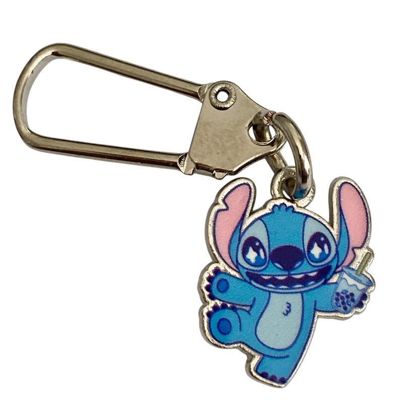 Puede incluir: Un llavero de Stitch azul y rosa con un cierre plateado. El personaje de dibujos animados sostiene una bebida. El llavero es un accesorio divertido para los fans de la pel&iacute;cula animada.