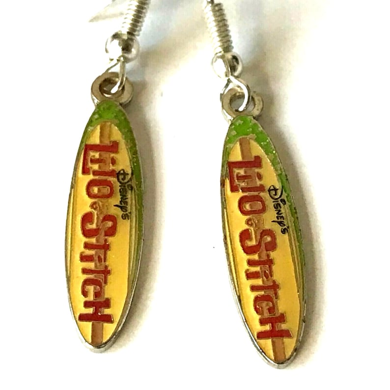 May include: A pair of silver Lilo & Stitch earrings featuring a surfboard design with the words "Disney's Lilo & Stitch" in red lettering on a yellow background.