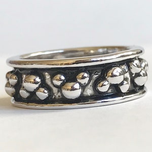 Puede incluir: Un anillo plateado con un patr&oacute;n repetido de formas de cabeza de Mickey Mouse. El anillo tiene un acabado pulido y una banda oscura y texturizada. El dise&ntilde;o es un motivo l&uacute;dico y reconocible, ideal para los fan&aacute;ticos del personaje ic&oacute;nico.