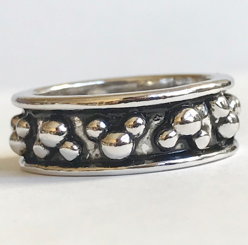 Puede incluir: Un anillo plateado con un patr&oacute;n repetido de formas de cabeza de Mickey Mouse. El anillo tiene un acabado pulido y una banda oscura y texturizada. El dise&ntilde;o es un motivo l&uacute;dico y reconocible, ideal para los fan&aacute;ticos del personaje ic&oacute;nico.