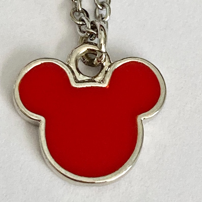 K&ouml;nnte beinhalten: Eine silberne Kettenkette mit einem roten Mickey-Maus-Kopf-Anh&auml;nger aus Emaille.