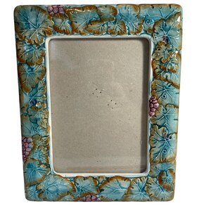 May include: A ceramic picture frame with a blue and green glaze. The frame is decorated with a raised design of leaves and grapes.