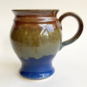 May include: A large, brown, green, and blue ceramic mug with a wide base and a rounded body. The mug has a large handle.