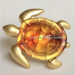 May include: A gold-colored turtle figurine with a translucent amber shell. The shell has a textured, cracked appearance.