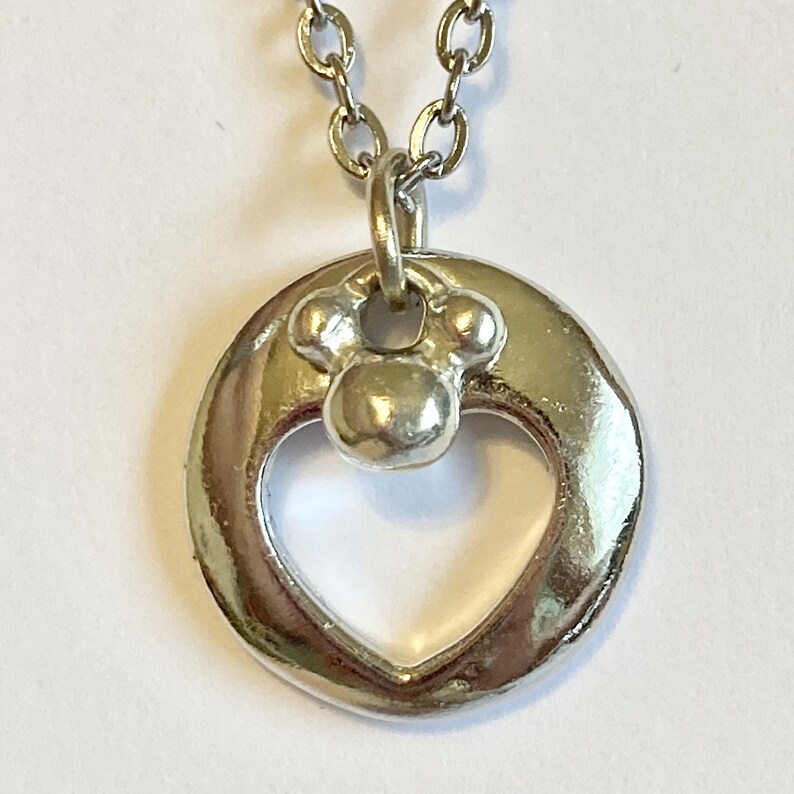 May include: Silver necklace with a heart-shaped pendant featuring a small paw print charm.