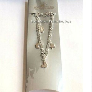 Puede incluir: Pulsera de plata con un dije de cabeza de Mickey Mouse, una luna creciente, una estrella y un c&iacute;rculo. La pulsera se muestra en una tarjeta blanca con el texto "Disneyland" y "South Miami Beach Boutique".