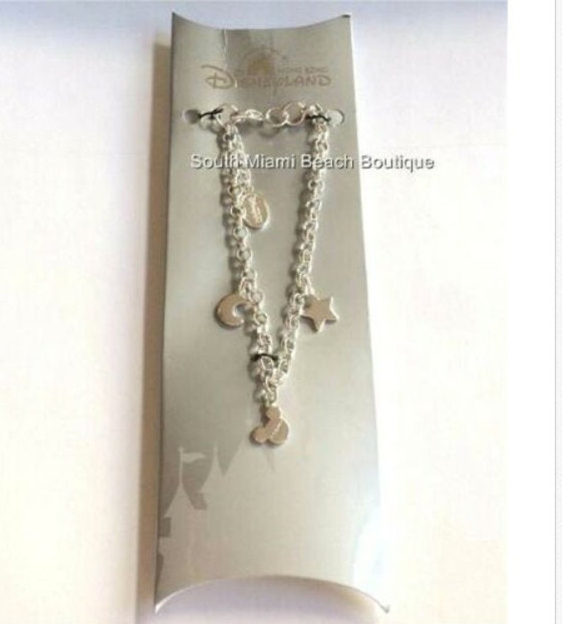 Puede incluir: Pulsera de plata con un dije de cabeza de Mickey Mouse, una luna creciente, una estrella y un c&iacute;rculo. La pulsera se muestra en una tarjeta blanca con el texto "Disneyland" y "South Miami Beach Boutique".