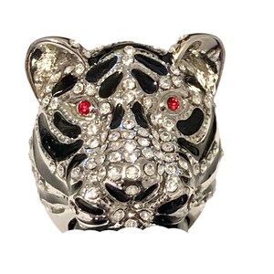 May include: A silver ring with a tiger head design. The tiger's eyes are red, and the ring is covered in clear rhinestones.