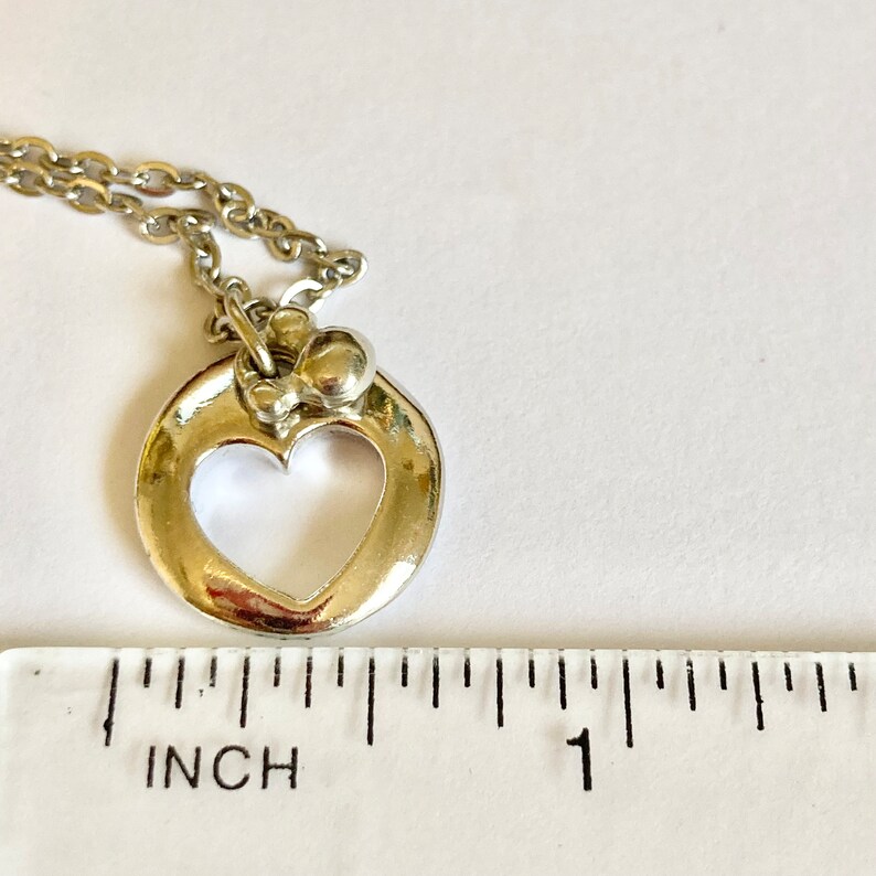 May include: Silver necklace with a heart-shaped pendant and a small bead detail. The pendant is about 1 inch in diameter.