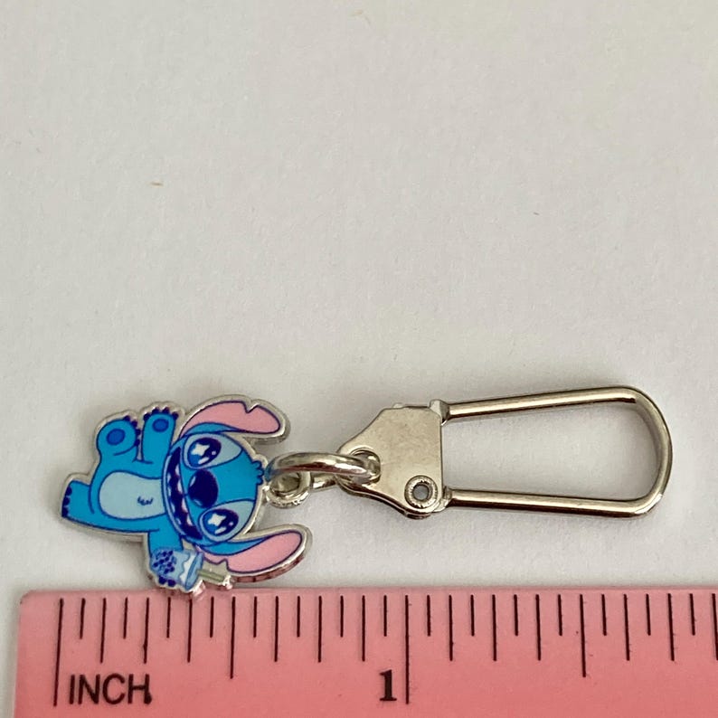 Puede incluir: Un charm de esmalte azul y rosa con el personaje Stitch de Lilo & Stitch. El charm est&aacute; unido a un cierre de mosquet&oacute;n de metal plateado. El charm mide aproximadamente 2,5 cm de largo.