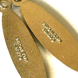 May include: Close-up of two gold-colored metal earring backs with the text "Made in Italy" and "925 Sterling" engraved on them.