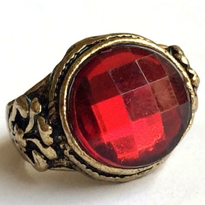 May include: A gold ring with a large, red, faceted gemstone. The ring has an ornate design on the band.