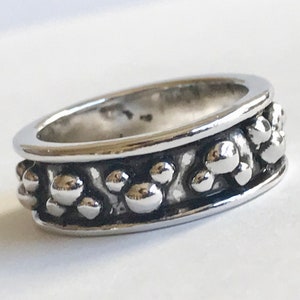 Puede incluir: Un anillo plateado con un dise&ntilde;o texturizado. El anillo presenta una banda de peque&ntilde;as formas esf&eacute;ricas en relieve alrededor de la circunferencia. El anillo tiene una superficie pulida y reflectante.