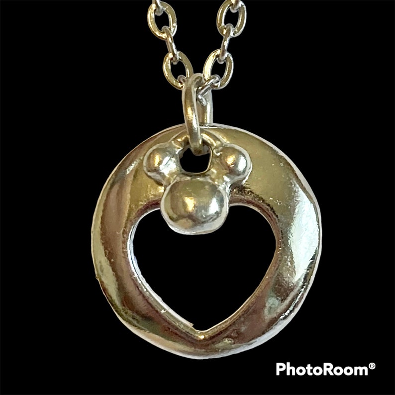 May include: A silver necklace with a heart-shaped pendant featuring a small Mickey Mouse charm. The pendant is attached to a silver chain.