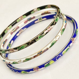 May include: Three enamel bangle bracelets with floral designs. The bracelets are black, white, and blue with green and pink accents.
