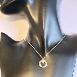 May include: A silver necklace with a heart-shaped pendant featuring a smaller heart cutout and a single clear rhinestone.
