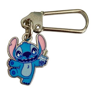 Puede incluir: Un charm de esmalte azul y rosa con el personaje Stitch de Lilo & Stitch, sosteniendo una bebida boba. El charm est&aacute; unido a un cierre de metal plateado, adecuado para un llavero o un accesorio de bolso.